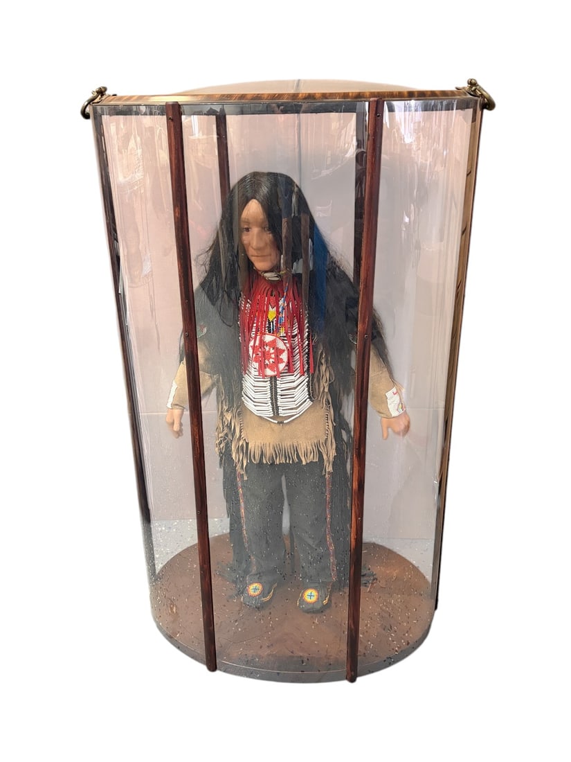 Native American Figure In Display Case Doll Statue: Life-size Native American figure or mannequin housed in a cylindrical display case. The case features a circular wood base, a domed curved glass top, and clear plastic side panels supported by wood up