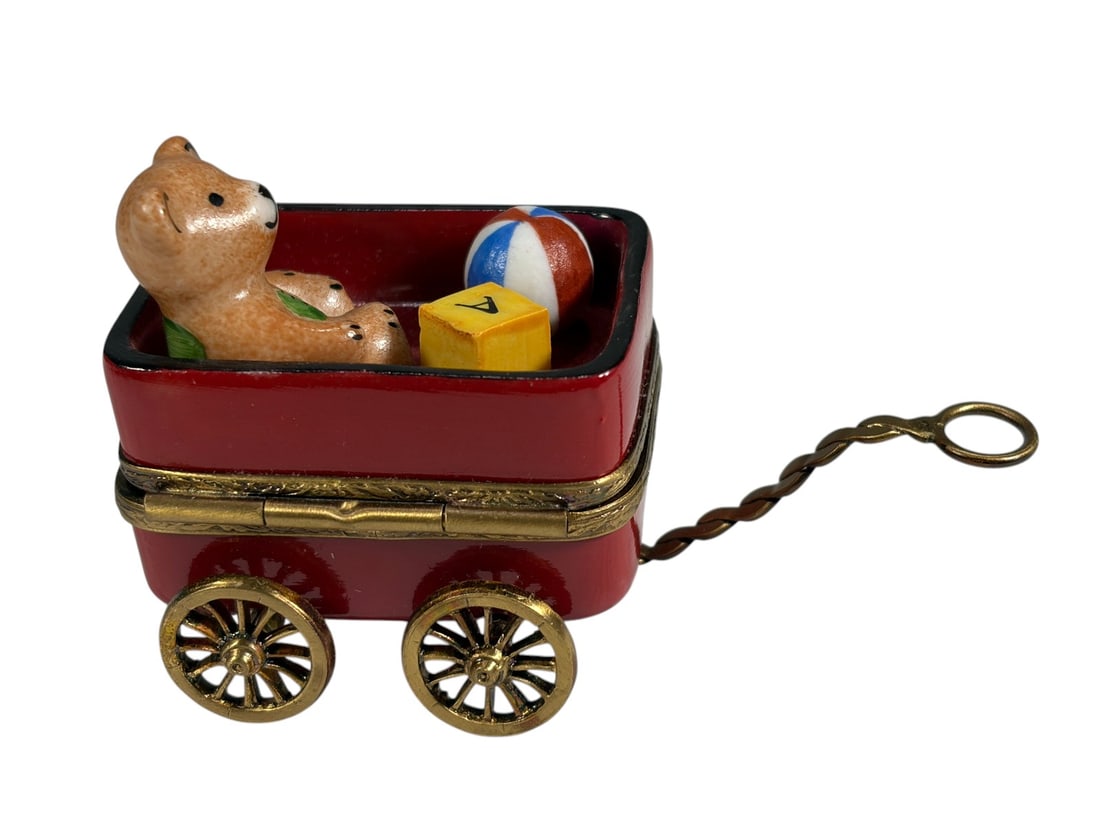 Limoges France Toy Wagon w/ Teddy Bear Trinket Box: Hand-painted Limoges porcelain trinket box modeled as a red toy wagon with brass-tone wheels and pull handle. The wagon contains a seated teddy bear, alphabet block, and striped ball rendered in relie