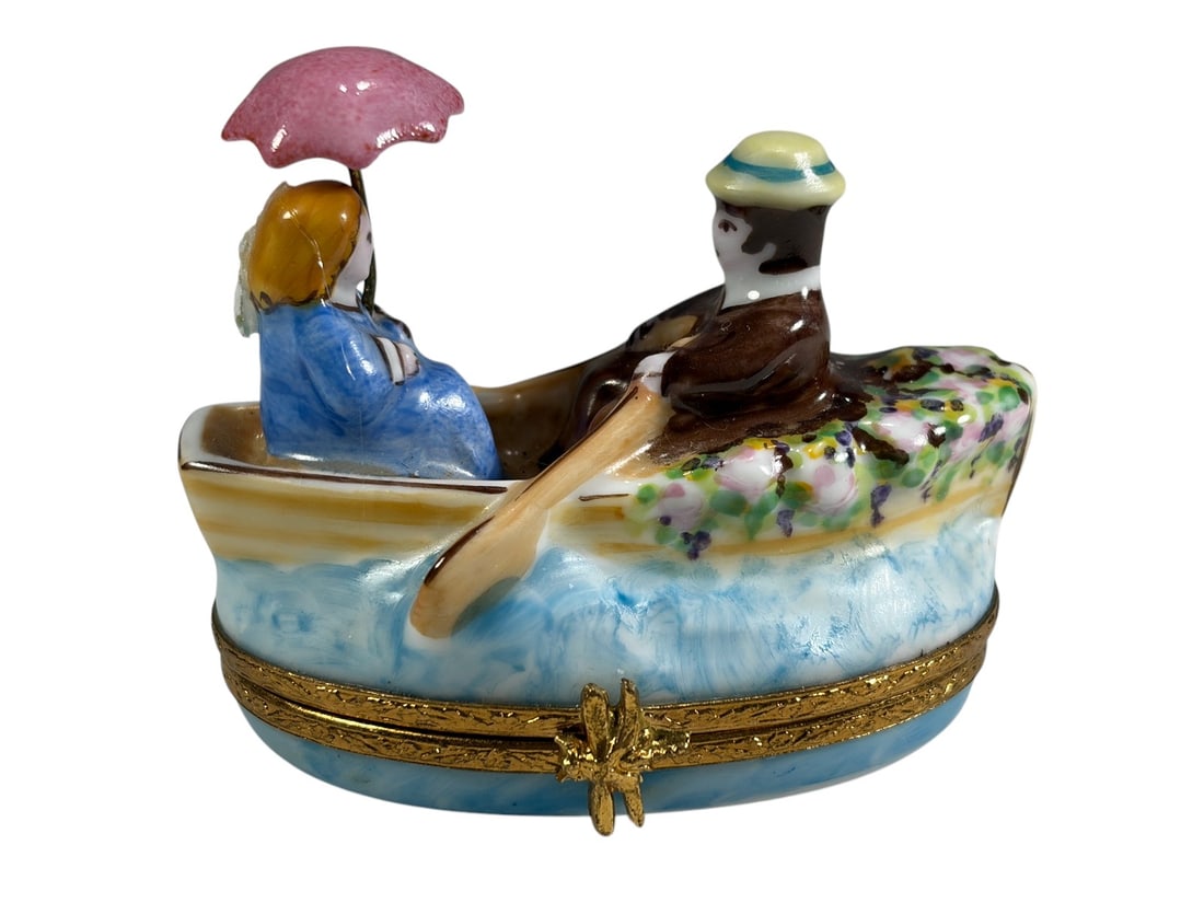 Artoria Limoges Romantic Rowboat Trinket Box: Hand-painted Artoria Limoges porcelain trinket box depicting a romantic couple seated in a rowboat. The gentleman rows while the lady sits beneath a pink parasol. The boat is decorated with floral sho