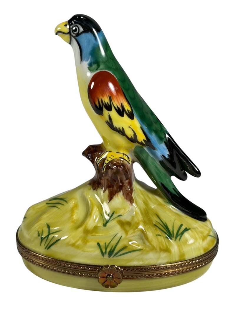 Limoges Porcelain Parrot Figural Trinket Box: Hand-painted Limoges porcelain trinket box featuring a colorful parrot perched on a tree stump atop an oval grassy base. The bird is decorated in shades of green, blue, yellow, red, and black with det