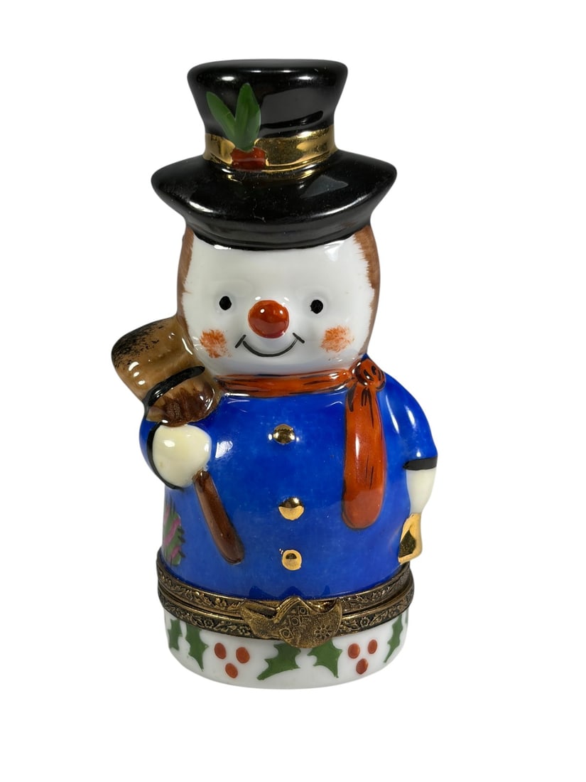 Limoges Porcelain Snowman Figural Trinket Box: Hand-painted Limoges porcelain figural trinket box modeled as a cheerful snowman wearing a black top hat with holly decoration, blue coat with gilt buttons, red scarf, and holding a broom. The hinged 