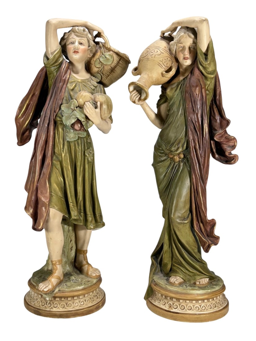Pair Royal Dux Bohemia Porcelain Maiden Figures: Pair of Royal Dux Bohemia porcelain figures depicting peasant maidens carrying water vessels. One figure carries a handled jug while the other carries a woven basket. Both are decorated in muted green