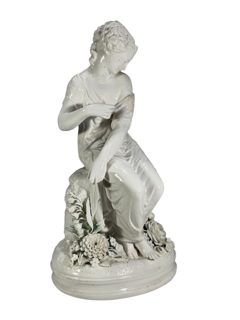 White Glazed Porcelain Maiden Figure Sculpture Art: White glazed porcelain figural sculpture depicting a seated maiden draped in flowing classical garments and surrounded by molded floral decoration. The figure is posed upon a naturalistic base with de