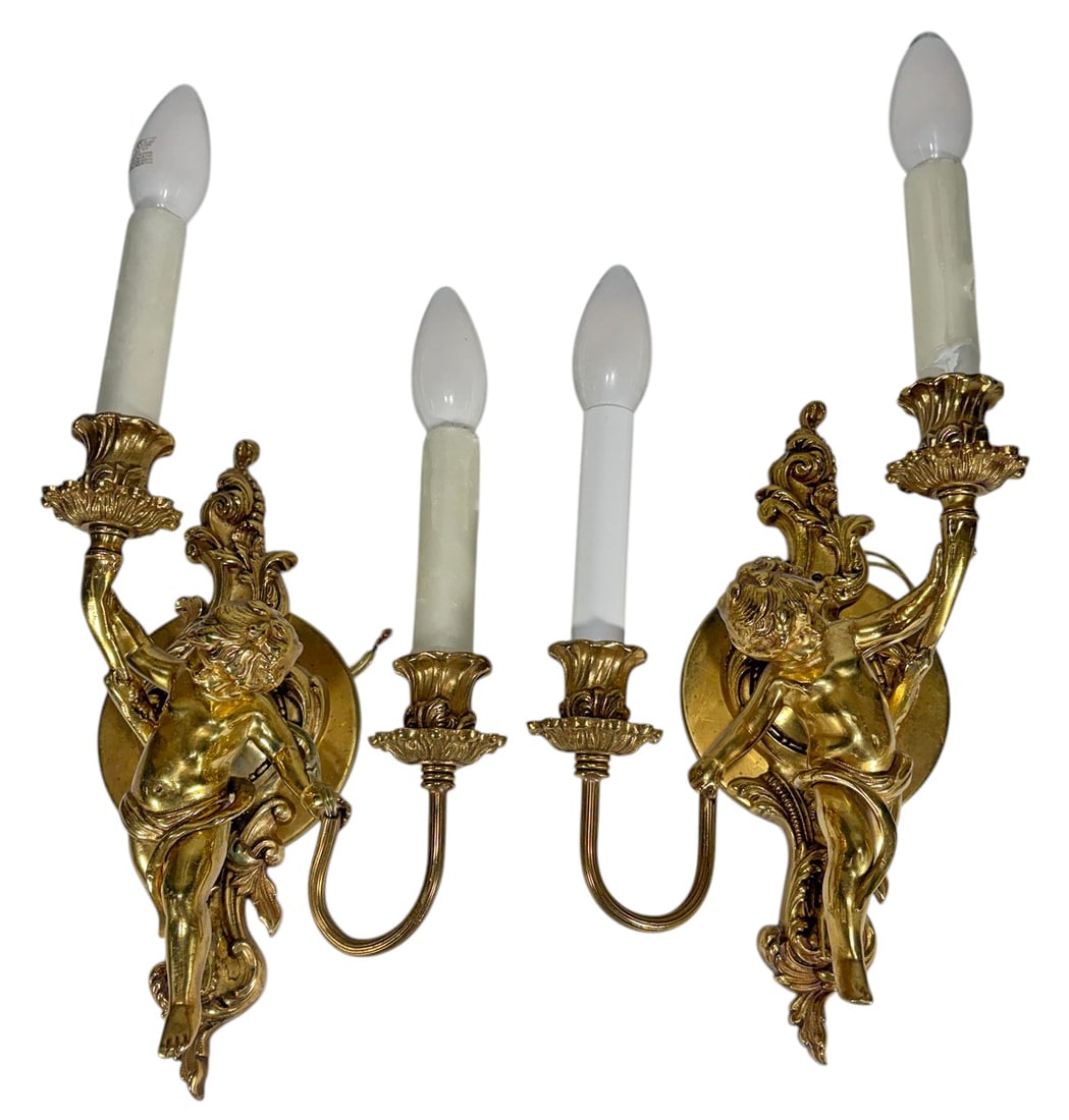 Antique Pair Bronze Cherub Two-Light Wall Sconces: Pair of matching bronze wall sconces featuring figural cherub mounts supporting two candle-form lights each. The sconces display ornate Rococo-inspired styling with scrolling arms, floral bobeches, an