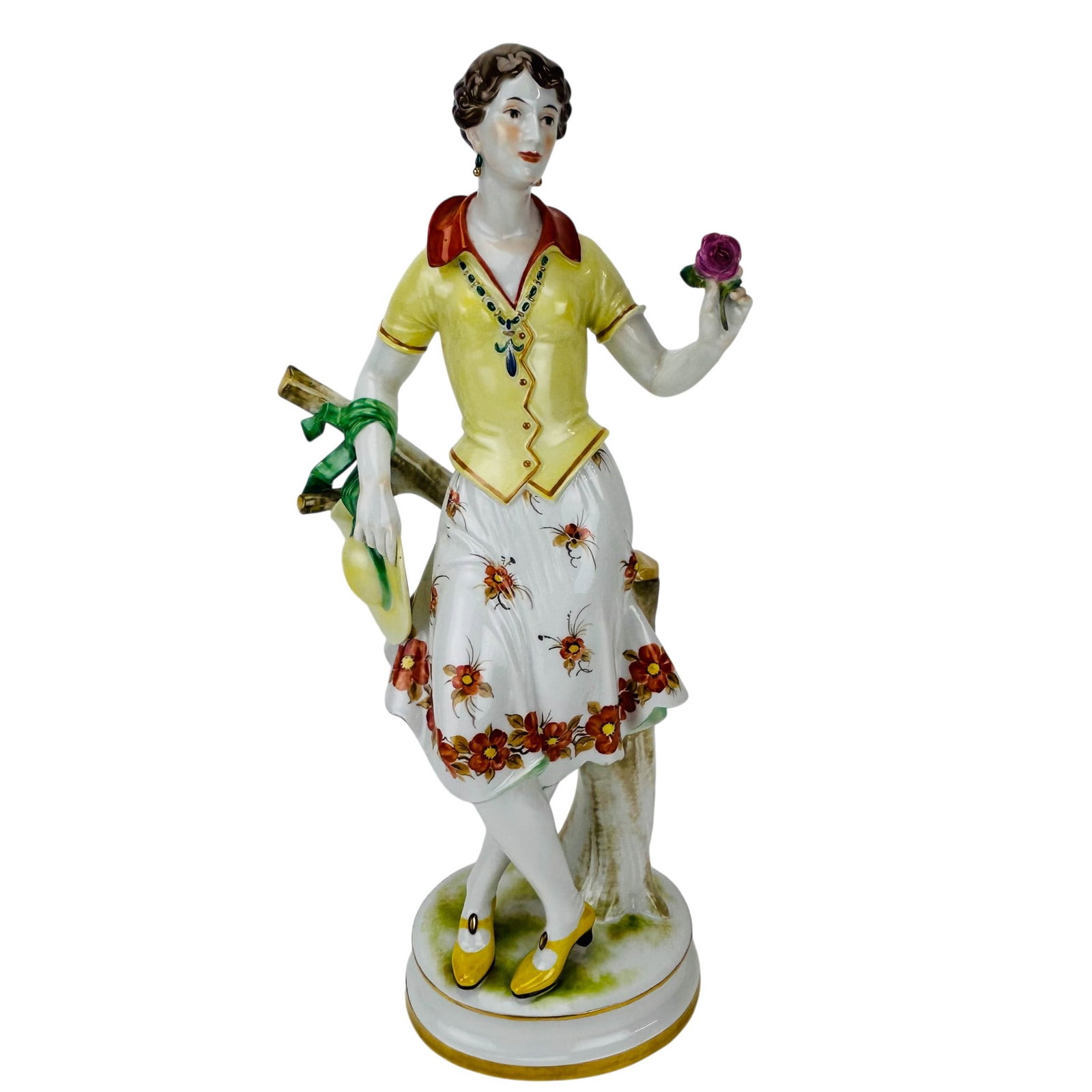 Oldest Volkstedt Porcelain Figurine Lady w/ Rose: German mid 20th century porcelain figure by Oldest Volkstedt. Depicting a lady in standing pose, holding a rose and hat beside a tree stump. Figurine modeled wearing a yellow blouse, floral skirt, and