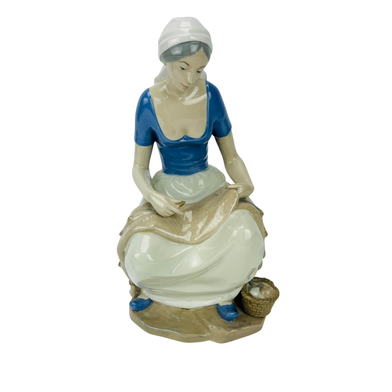 REX Porcelain Figure of Woman Mending Fishing Net: Spanish Lladro-style porcelain figural sculpture depicting a seated young woman mending a fishing net. The figure is modeled in a traditional fisherfolk costume with blue bodice, white skirt, and head