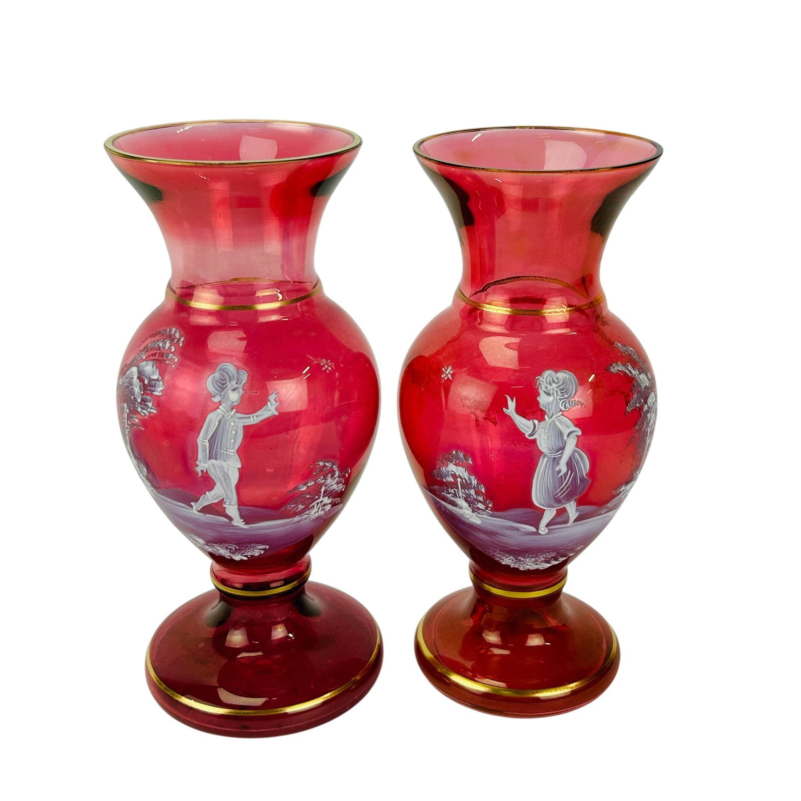 Bohemian Ruby Red Glass Mary Gregory Vases 2pc LOT: Pair of Bohemian Czech cranberry art glass vases, each of baluster form with flared rim and circular foot. Decorated in the Mary Gregory style with white enamel figural scenes depicting a young boy an