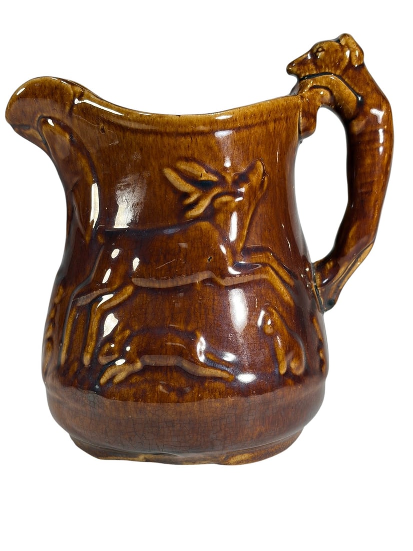 Rockingham Glazed Bennington Hound Handle Pitcher: Rockingham Bennington brown glazed pottery pitcher featuring molded hunting scene relief decoration with rabbits and hounds. The sculptural handle is formed as a hound, with a shaped pouring spout and