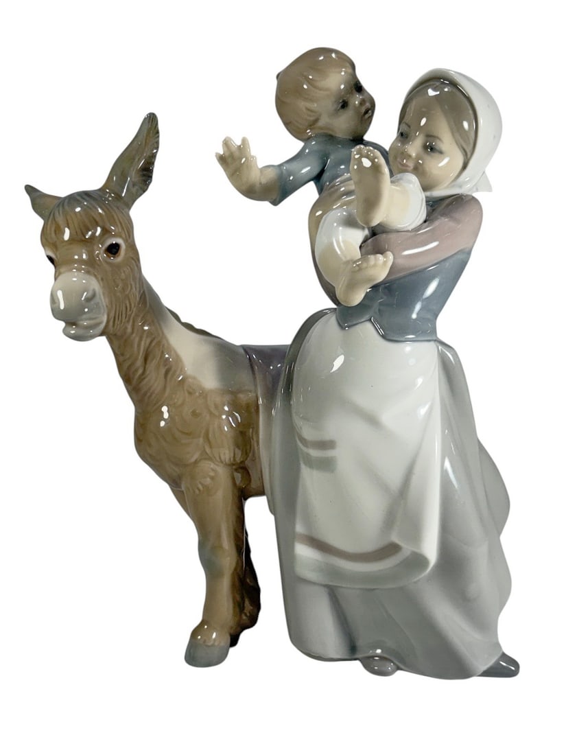 Lladro Figurine Girl Child Donkey Porcelain Spain: Lladro porcelain figurine depicting a young girl carrying a child beside a donkey, finished in the maker's characteristic soft pastel glaze. Marked Lladro Hand Made in Spain on the underside. A charmi