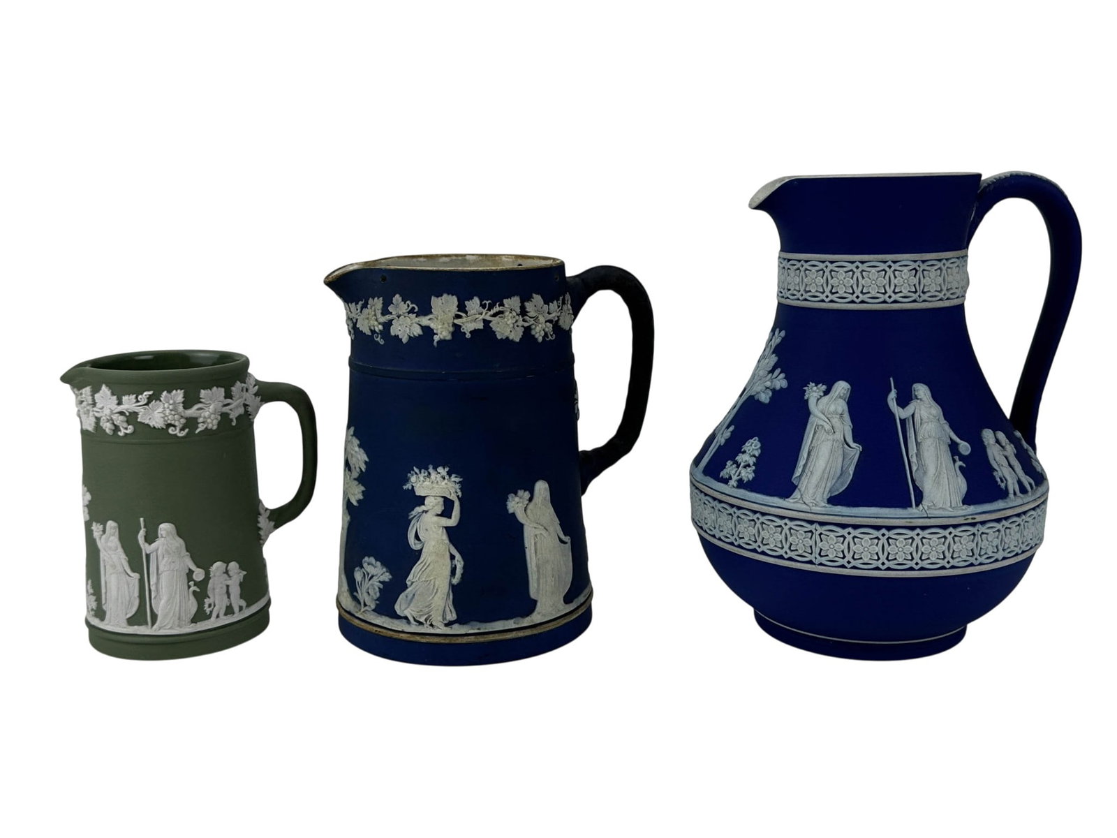 Wedgwood Blue & Green Jasperware Pitcher Jugs LOT: Collection of three Wedgwood English Jasperware ceramic pitchers in cobalt blue and sage green. Included are a large Portland Blue pitcher with white classical relief depicting draped figures, cherubs