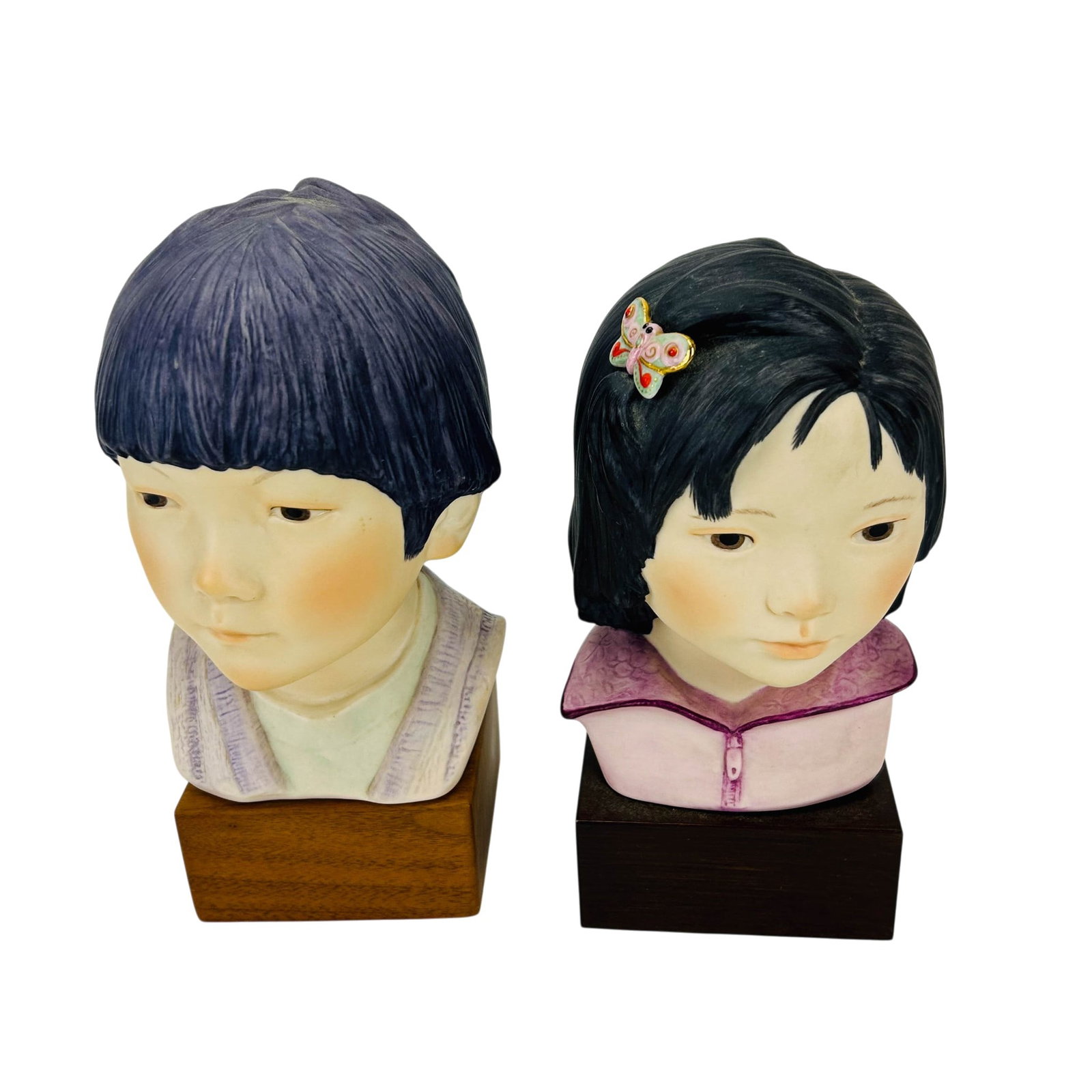 Cybis Pair of Porcelain Boy and Girl Portrait Bust: Pair of Cybis porcelain portrait busts. Depicting Lotus Blossom, a girl with a butterfly hair ornament and a Cheerful Dragon, a boy with a bowl-cut hairstyle. Each mounted on a fitted wood display pli