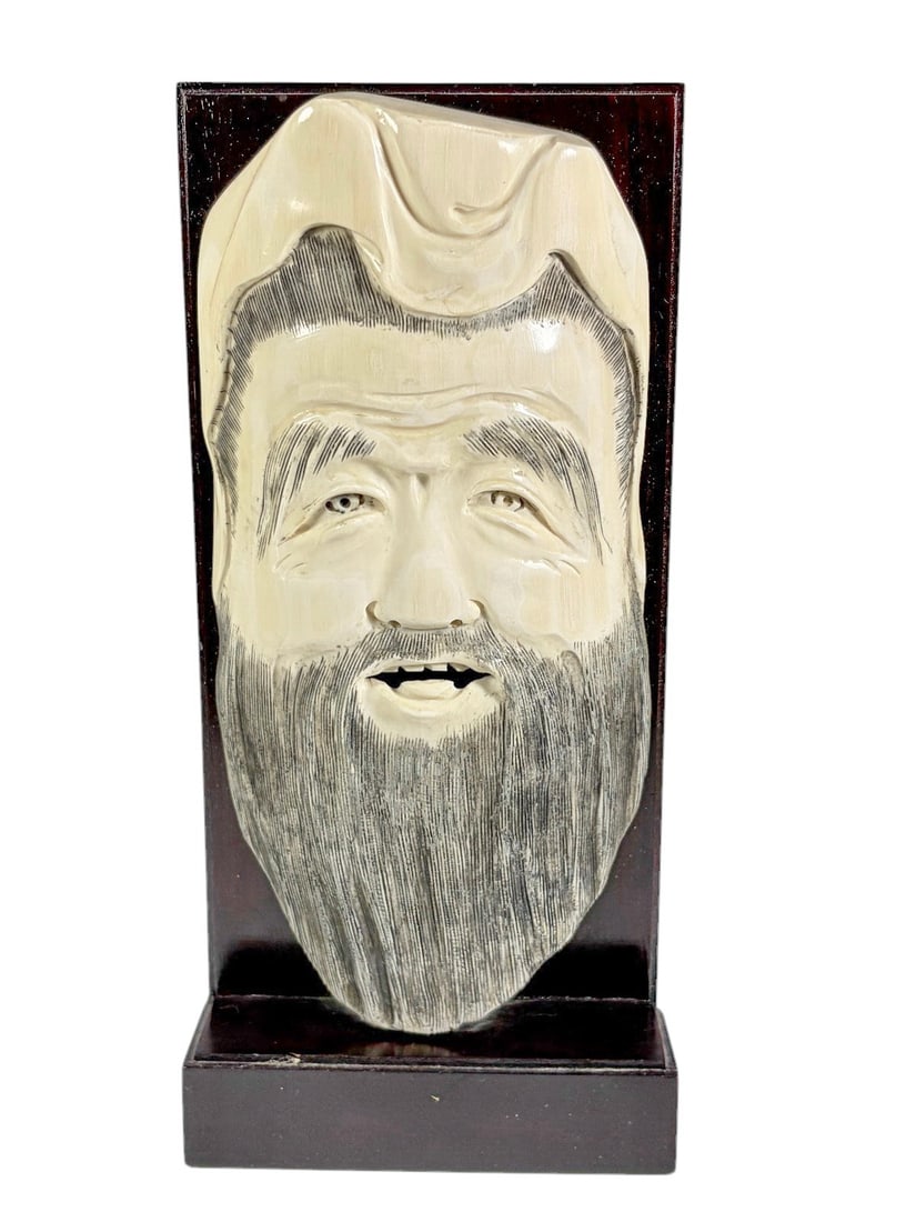 Carved Asian Bearded Male Wall Plaque Wood Mounted: Decorative carved Asian wall plaque depicting a smiling bearded male figure wearing a traditional headdress. Executed in a cream-colored carved material with finely incised facial features and beard d