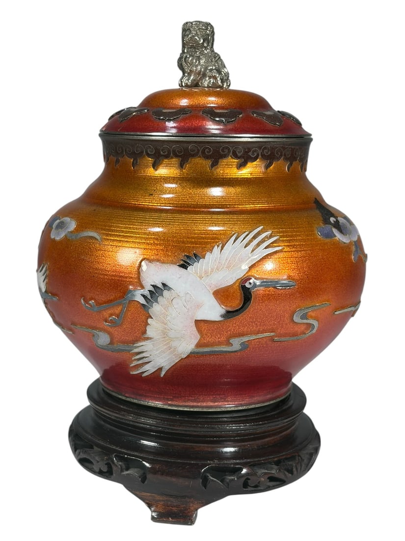 Japanese Ando Jubei Style Enamel Jar w Stand Lid: Japanese Ando Jubei style enamel jar and cover with carved wood stand. Decorated with flying cranes against an orange-red guilloche enamel ground and topped with a shishi finial. Includes fitted