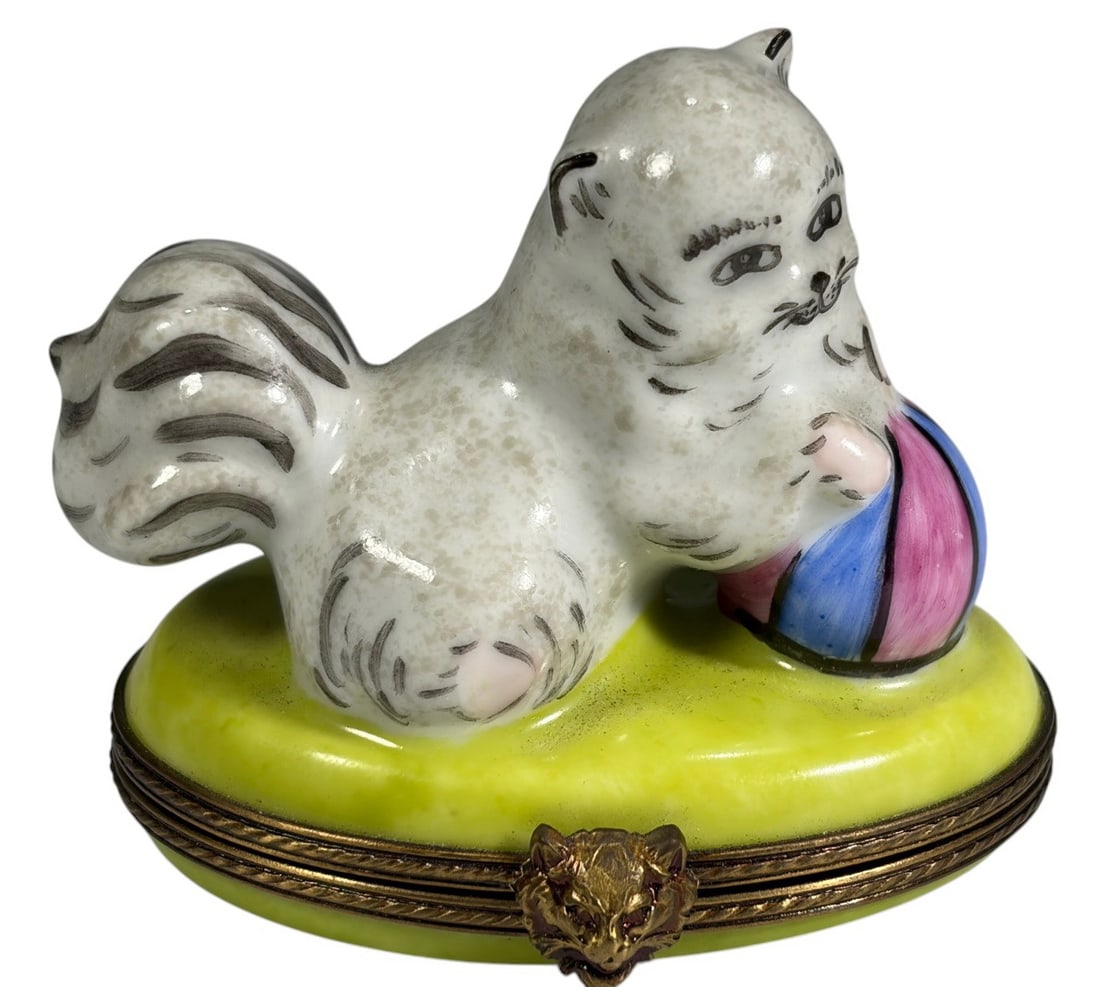Limoges Kitten Playing Ball Hinged Trinket Box: French hand-painted Limoges porcelain hinged trinket box modeled as a fluffy kitten playing with a colorful striped ball on an oval base with gilt metal mounts. Interior decorated with a hand-painted 