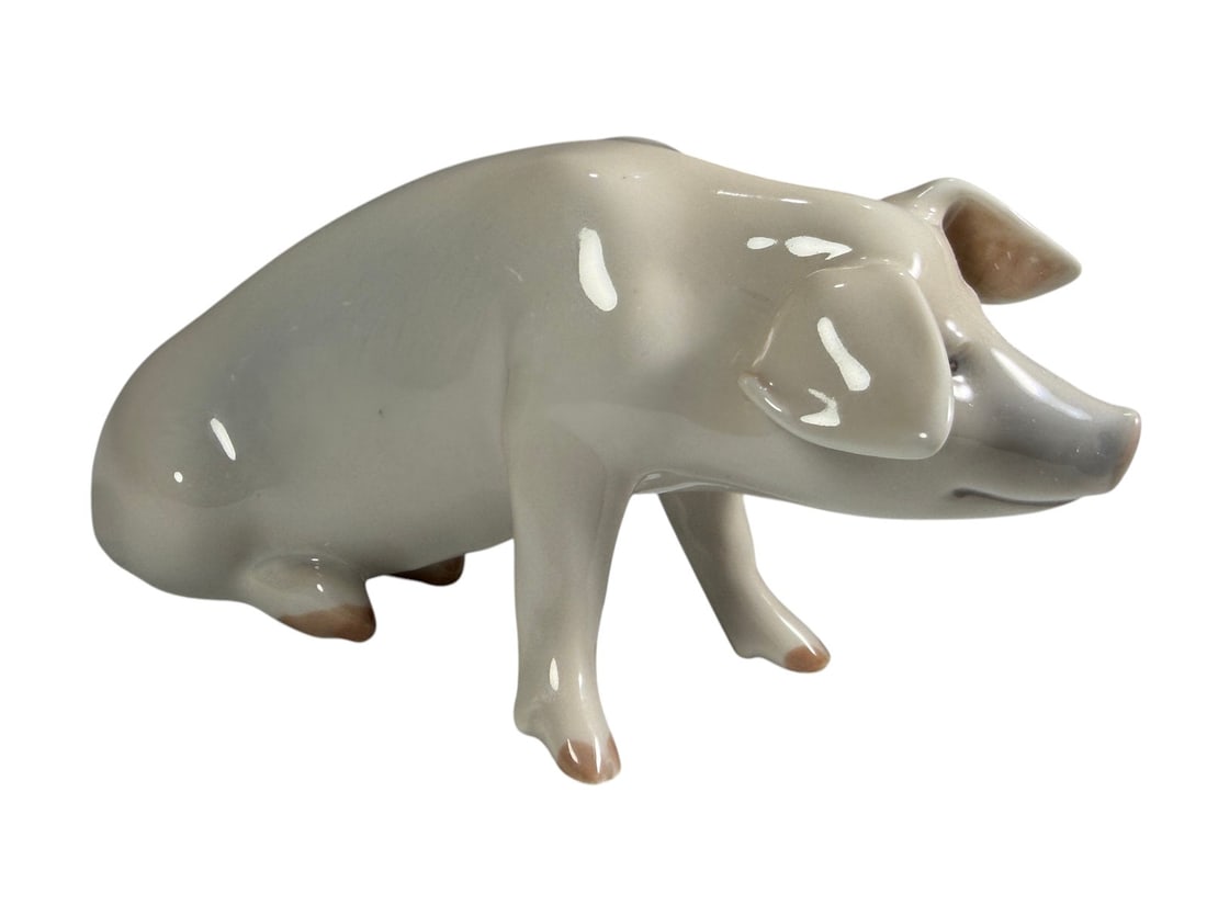 Royal Copenhagen Porcelain Pig Figure: Royal Copenhagen porcelain figure depicting a standing pig with a glossy white glaze and pale pink accents to the snout, ears, hooves, and tail. Marked Royal Copenhagen Denmark on the underside with t