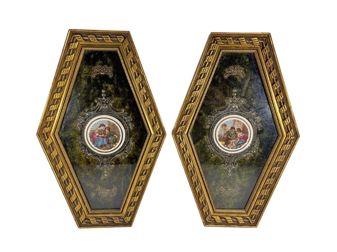 Pair of Gilt Framed Porcelain Scenic Genre Plaques: A pair of decorative wall plaques featuring small round porcelain medallions with colorful European-style genre scenes. Each medallion is mounted within an ornate metallic scrollwork surround on a dar