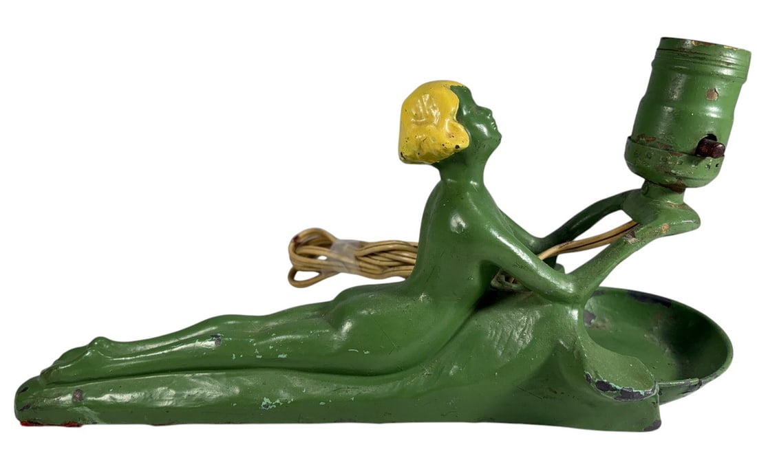 Art Deco Painted Female Figural Metal Table Lamp: Vintage Art Deco-style figural table lamp featuring a reclining female figure with painted blonde hair, finished in green-painted metal. The figure holds an upright light socket above an integrated ci