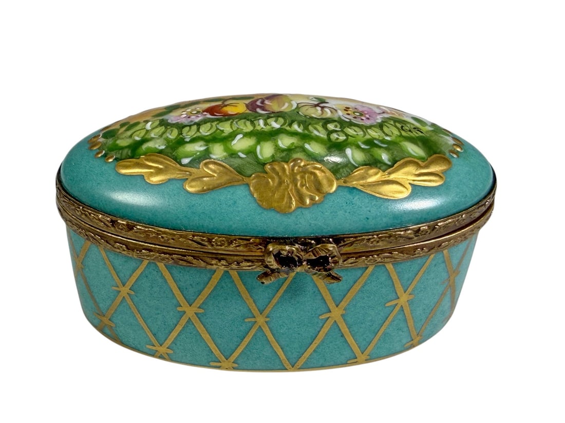 Limoges France Glorette Fruit Hinged Trinket Box: Hand-painted Limoges porcelain hinged trinket box by Glorette, decorated with a turquoise ground, gilt lattice accents, raised gilt floral ornament, and a colorful still life of fruit and flowers on t