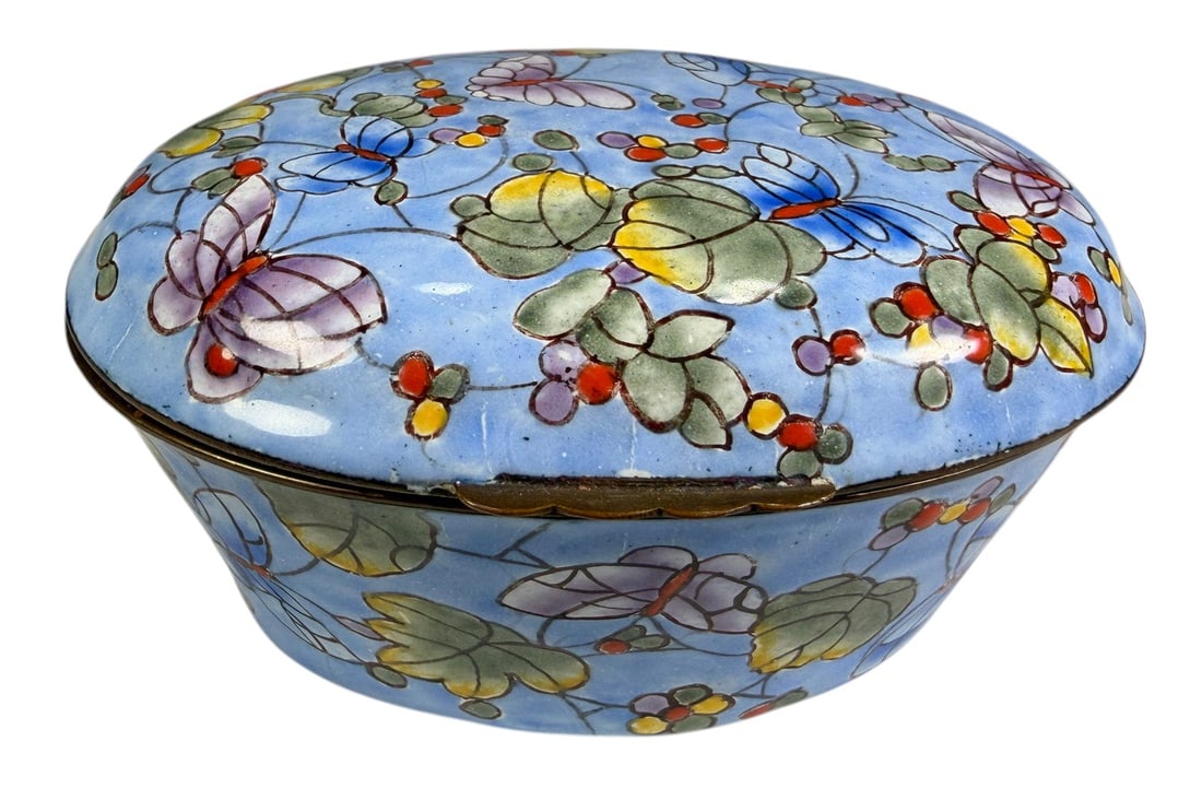 Colorful Floral Enamel on Metal Hinged Trinket Box: Oval hinged trinket box crafted in enamel over metal, decorated with a pale blue ground and colorful floral and foliate motifs in green, yellow, red, purple, and blue. The rounded lid and sides are fu