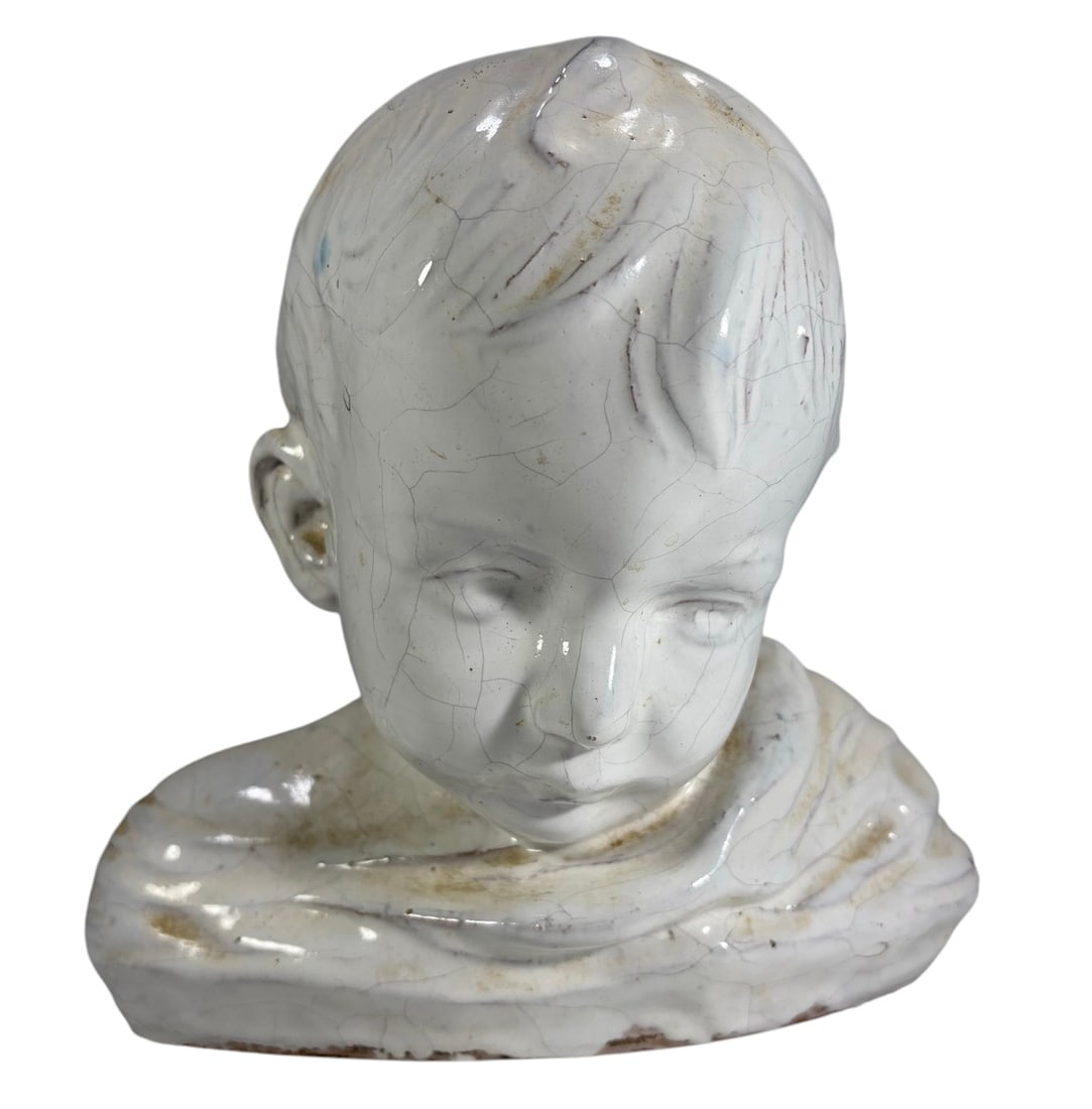 White Glazed Ceramic Child Bust Sculpture: White glazed ceramic bust sculpture depicting a young child with stylized facial features, molded wavy hair, and a draped garment. Hollow construction with an elongated oval base. Unmarked. Dimensions
