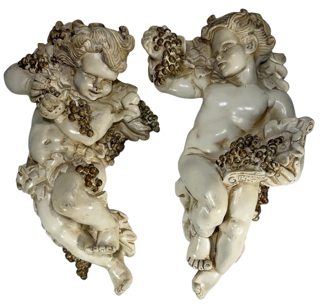 Composition Figural Putti Wall Plaques 2pc LOT: Two-piece lot of decorative composition wall plaques depicting reclining putti or cherubic figures with grape clusters, foliate decoration and classical-style drapery. Each is finished in an ivory