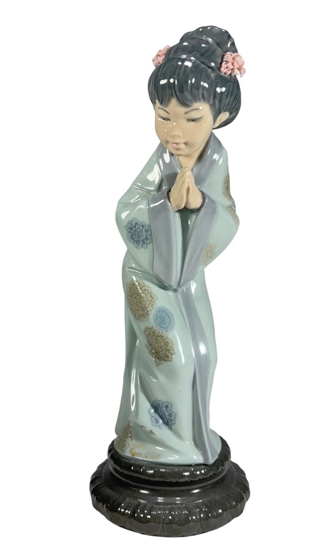 Lladro Spain Sayonara Geisha Porcelain Figurine: Lladro porcelain figurine titled Sayonara, depicting a Japanese woman or geisha bowing with her hands clasped, wearing a pale blue kimono decorated with floral motifs and a darker blue obi. Her hair