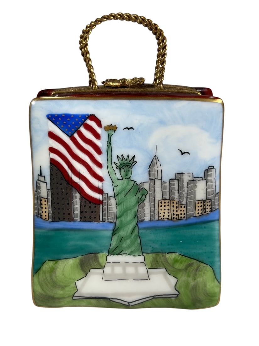 Limoges France New York Handbag Trinket Box: Whimsical hand-painted Limoges France porcelain trinket box modeled as a red handbag with a twisted gilt metal handle. One side features the Statue of Liberty, New York skyline, and American flag, whi