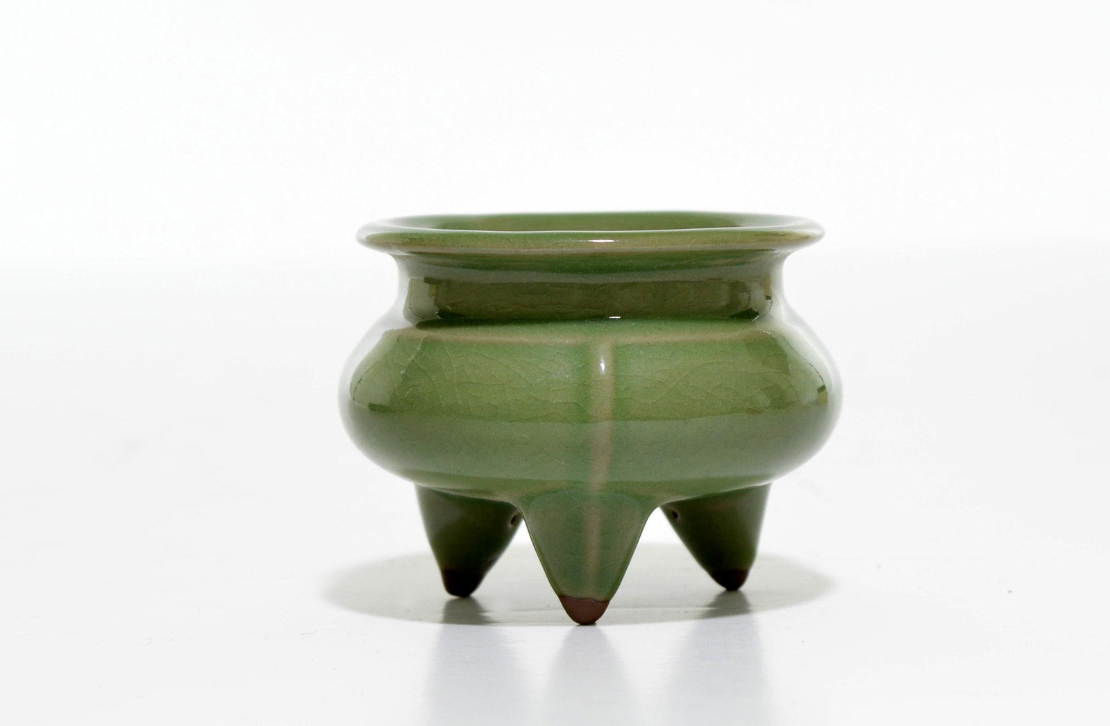 A Fine Chinese Celadon Tripod Porcelain Burner: Compressed body supported on three finely carved legs and surmounted with aa short neck and an everted mounthrim, covered overall with rich seaweed-green tone of glaze. Early Ming dynasty. D: 3 INCHES