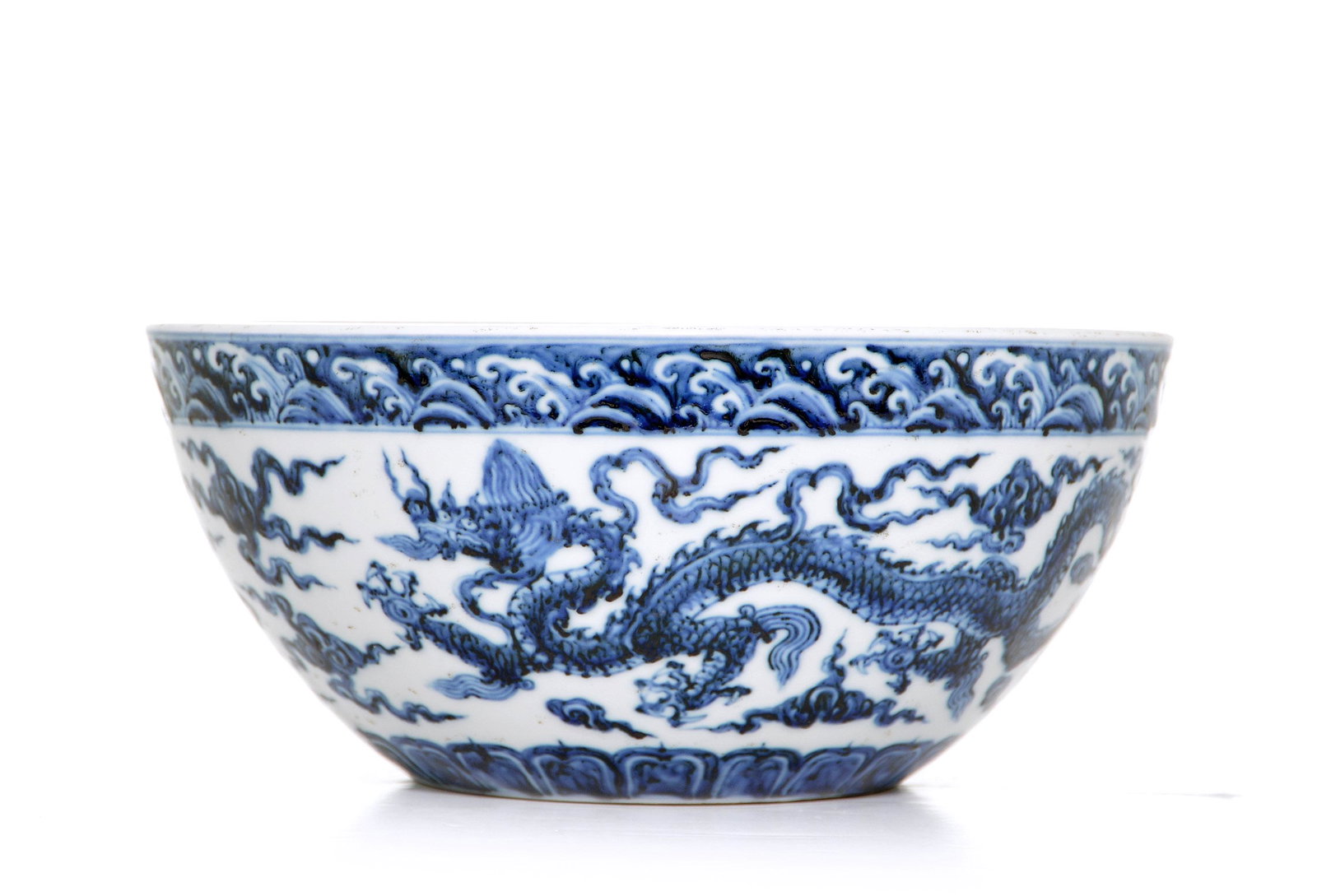 A Rare Chinese Blue and White Bowl: Stoutly potted bowl painted in underglaze-blue of very strong inky-blue tones and decorated with two ferocious dragons amidst scattered clouds below band of cresting waves. D: 27.5 cm