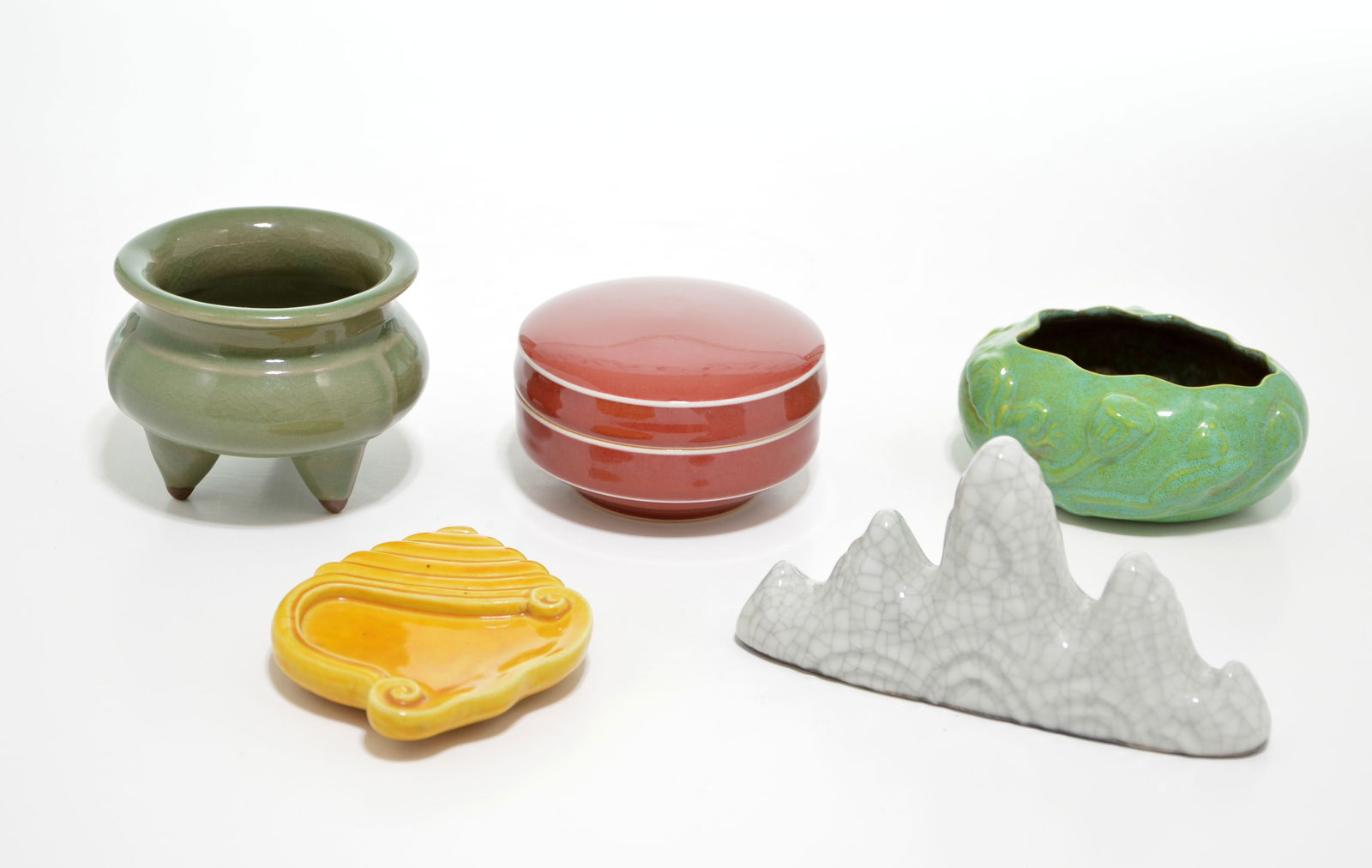 Group of Chinese Scholar Items: Consists of five distinct pieces featuring various traditional glazes and forms, including a copper-red circular ink-paste box and cover, a small Longquan-type tripod censer, and an archaistic Ge-type