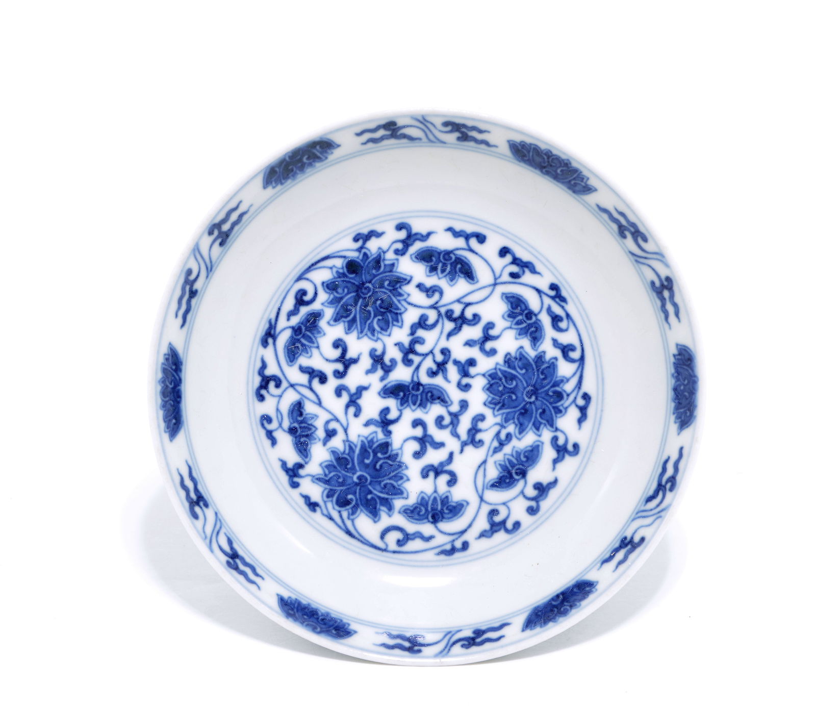 Chinese Blue and White 'Lotus' Dish: The shallow circular dish with rounded sides and a flared rim, the interior centrally decorated with a large medallion of interlocking lotus blooms and formal scrolling foliage. The design is