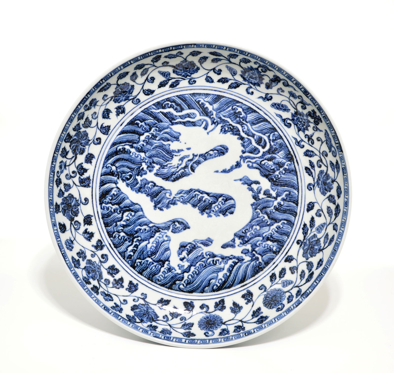 Magnificent Chinese Blue and White 'Dragon' Dish: Powerfully decorated in the early Ming style, featuring a dynamic, white-reserved dragon writhing amidst roiling, cresting waves. The interior well is centered by this monumental celestial creature,