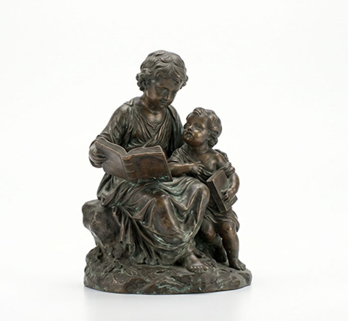 Bronze Group of Reading Children: Bronze statue depicting an older child reading an open book to a younger child sitting alongside. The figures sit on a naturalistic base and are dressed in simple draped clothing. H: 12 cm