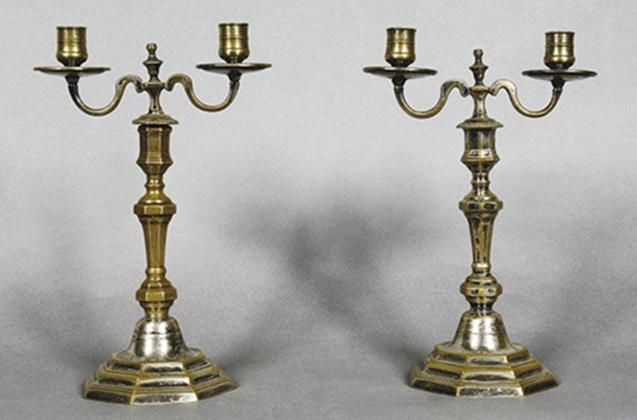 A Pair of Brass Candelabra: Pair of brass two-arm candlesticks with hexagonal bases and faceted stems. Each branch supports a candle cup resting on a round drip pan. The metal finish displays signs of aging and wear across the