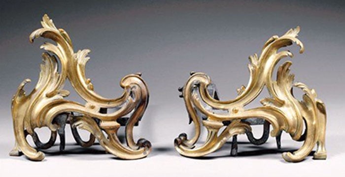 Louis XV Style Ormolu Chenets: Brass fireplace andirons feature asymmetrical scrollwork and leaf patterns. Darker metal supports are attached to the back of the decorative fronts. Surface wear is visible across the metal