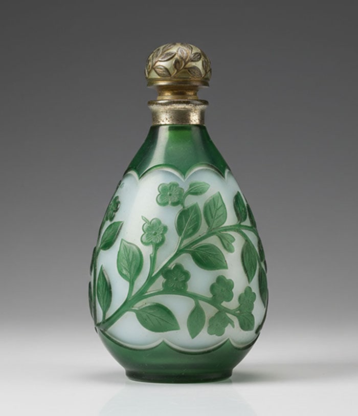 Green Overlay Cameo Scent Bottle: Glass bottle with green floral designs carved over a white translucent surface. The neck and stopper are constructed from white metal and decorated with small leaves. H: 27 CM