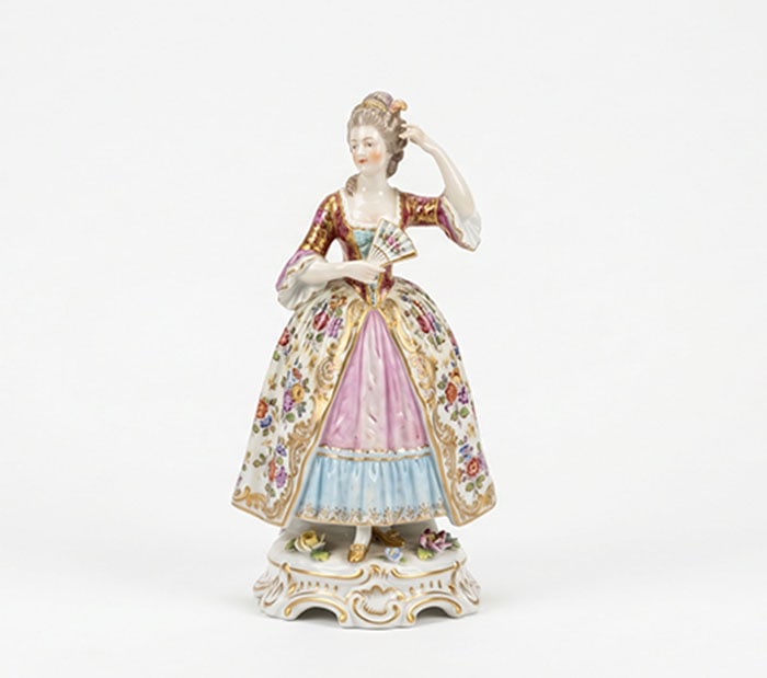 An Elegant Porcelain Lady: Ceramic figurine depicting a woman in a floral dress with brass accents holding a fan. H: 14 cm