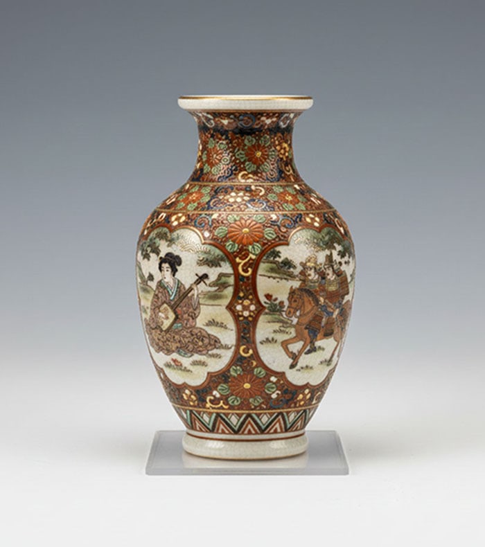 Japanese Satsuma Earthenware Vase: Ceramic vase decorated with panels of figures and floral patterns. Brass accents are applied over a cream-colored crackle glaze. The vessel has a flared neck and a rounded body. H: 26 CM