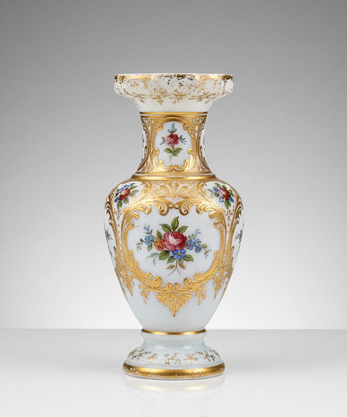 Gilt and Floral Porcelain Vase: White ceramic vase decorated with floral paintings and brass-colored accents. The vessel features a flared rim, a narrow neck, and a wider body tapering to a circular base. Floral motifs in pink,