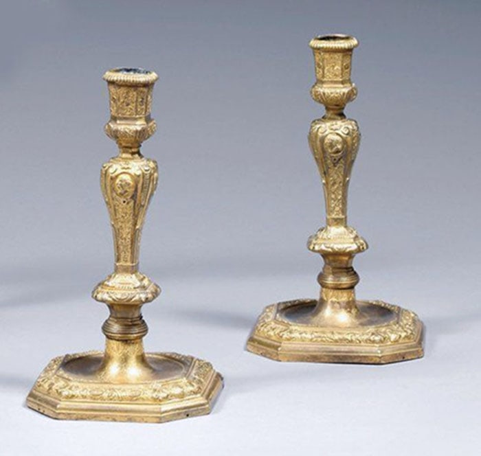 Pair of Gilt-Bronze Candlesticks: Brass candle sticks featuring hexagonal bases and decorative shafts. Surface patterns are visible across the exterior of both metal objects. Each piece is designed to hold one candle. H: 18 CM