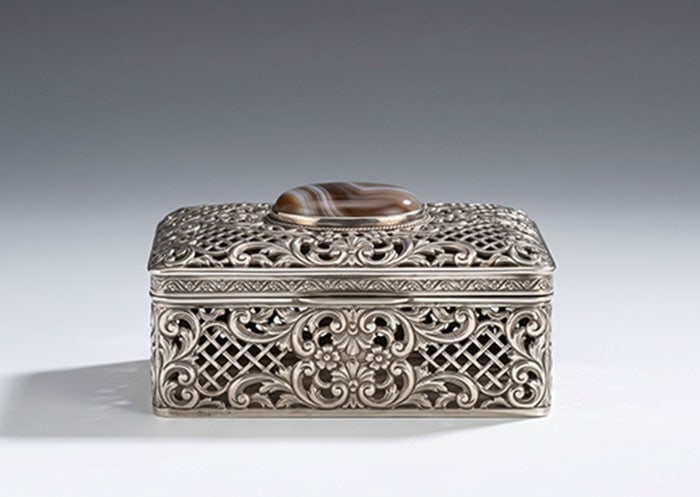 White Metal and Agate-Mounted Casket: Rectangular white metal box features an openwork lattice and scroll pattern on its sides and lid. A brown and white polished stone is set into the center of the top. L: 14 CM