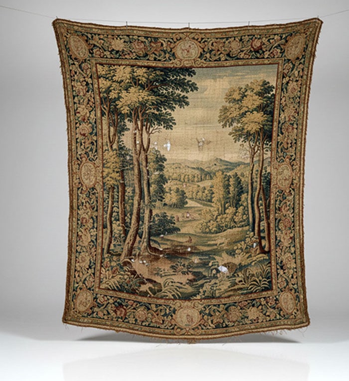Fine Tapestry: Woven tapestry wall hanging featuring a forest landscape with tall trees and a wide border of floral designs. The textile shows a scene of rolling hills and a small village in the distance. L: 163 CM