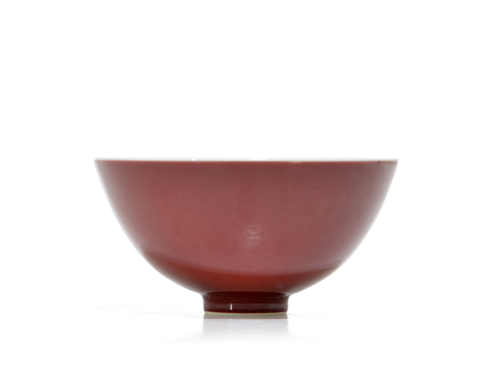 Rare Chinese Copper-Red Ceramic Bowl: Ceramic bowl featuring a deep red glaze on the exterior surface. The bowl has a tapered profile resting on a narrow circular base. A white glaze is visible along the top rim and within the recessed