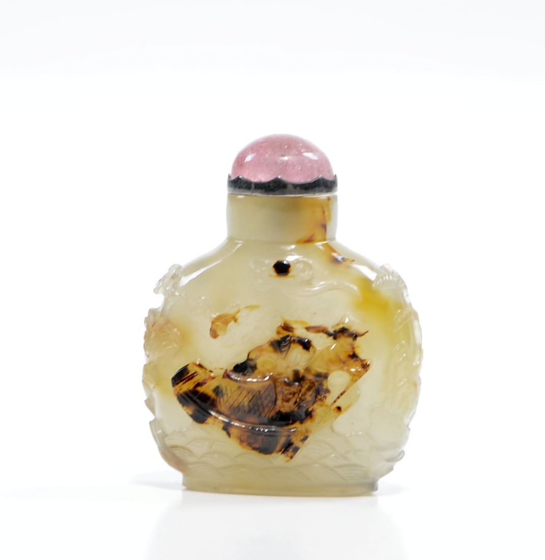 Chinese Carved Agate Snuff Bottle: Agate snuff bottle of compressed globular form, expertly carved in relief to utilize the natural dark inclusions of the stone, depicting a figure navigating a vessel amidst turbulent waves. The sides 