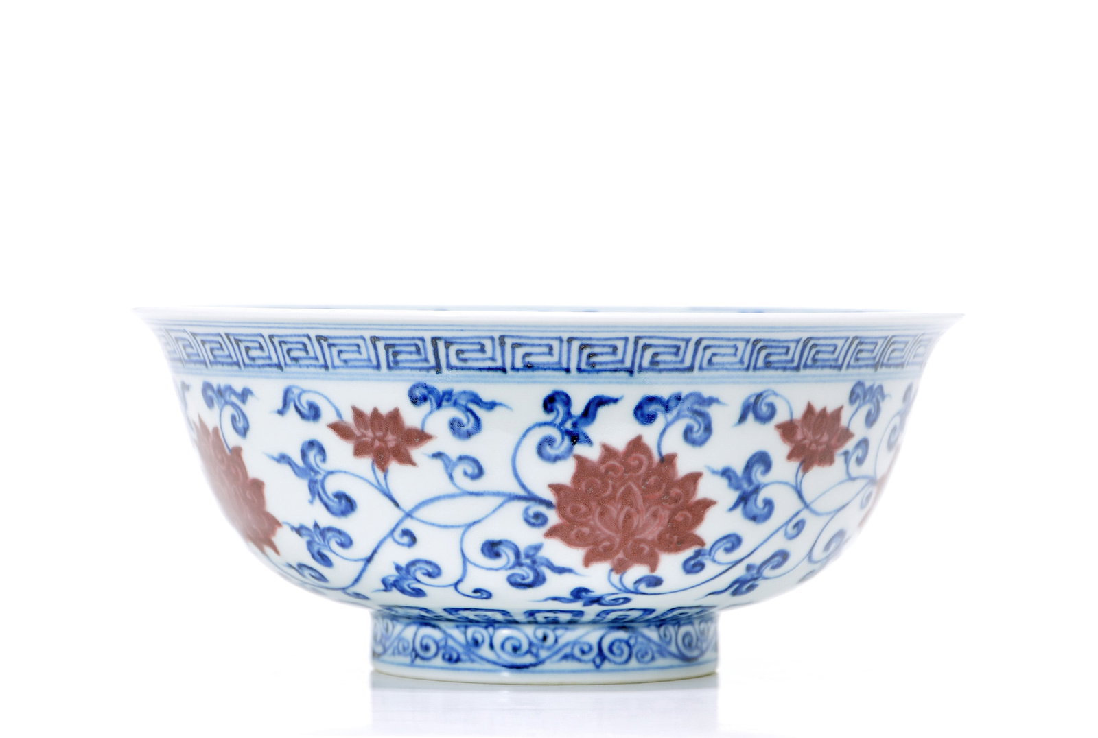 Chinese Copper-Red Decorated 'Lotus' Bowl: Bowl exquisitely potted with a flared rim, the exterior decorated in underglaze blue and red with a continuous scroll of lotus blossoms among dense leafy tendrils. A classic key-fret border encircles