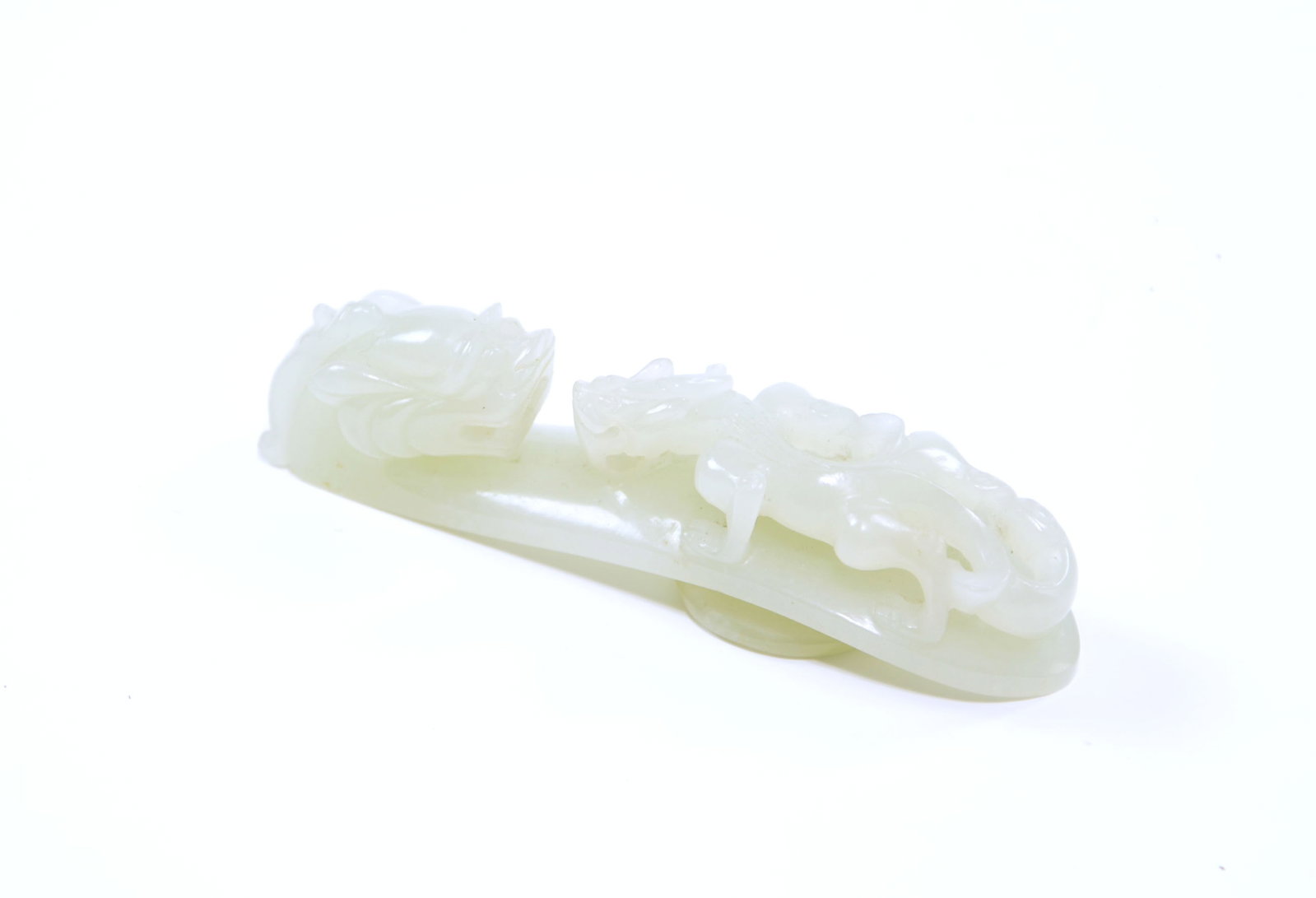 Chinese Jade Dragon Belt Hook: Belt hook of pale celadon jade masterfully carved with a powerful dragon head terminal featuring bulging eyes and a swept-back mane. The arched shaft is further embellished with a smaller, sinuous chi