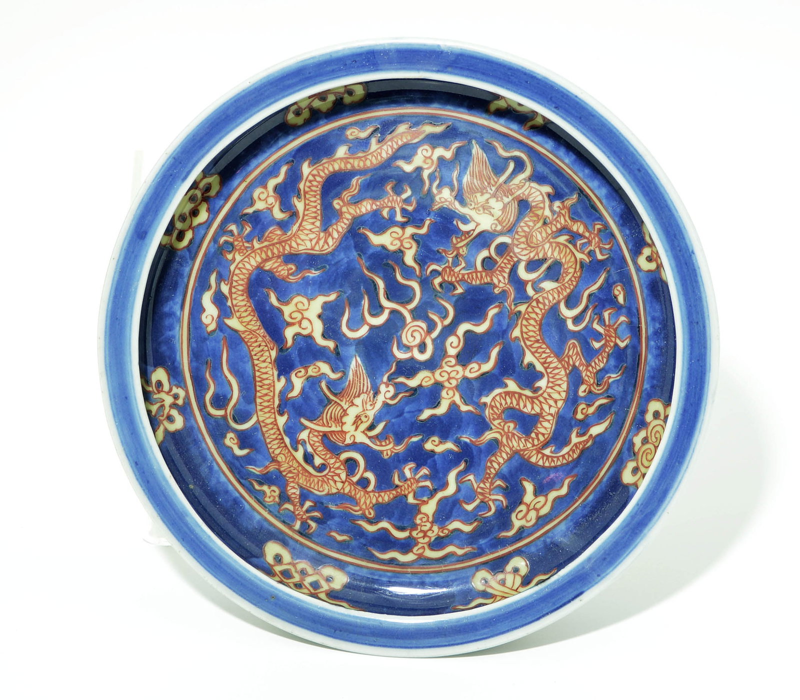 Rare Chinese Longqing Iron-Red Dragon Dish: Dish of shallow circular form, the interior finely decorated with two vigorous dragons writhing amidst ruyi-head clouds and stylized flames against a deep cobalt blue ground. The exterior continues th