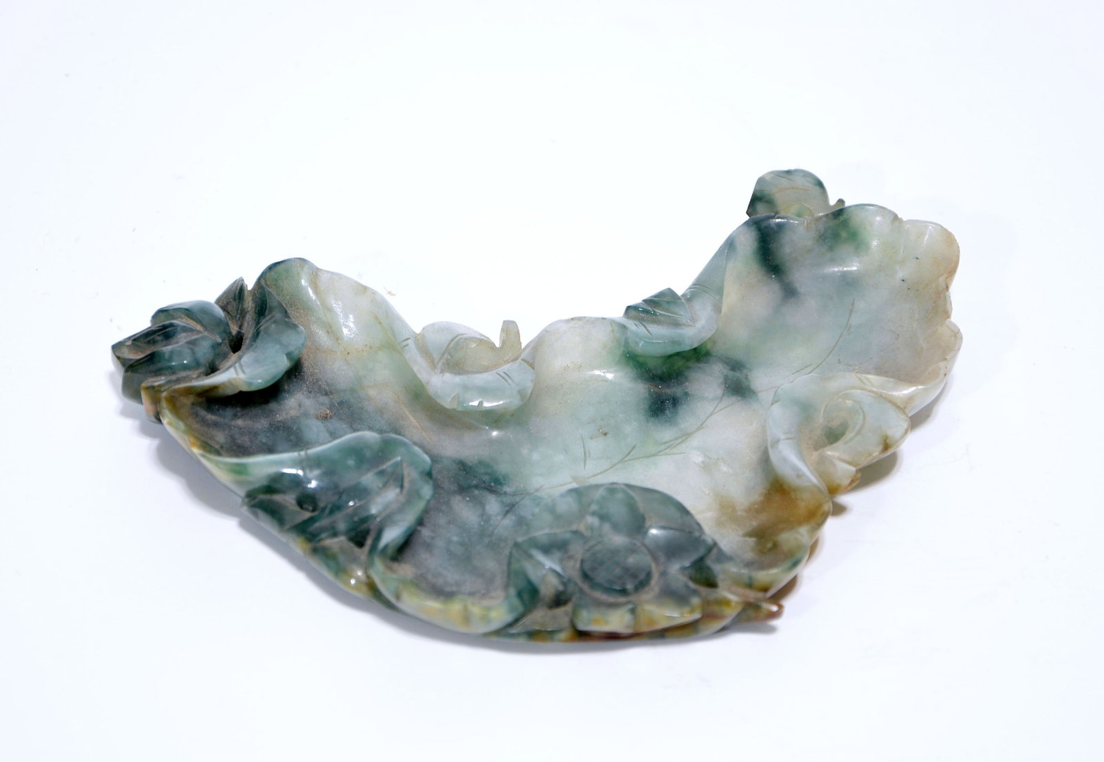 Chinese Jadeite Brush Washer: The shallow washer is carved as a curling lotus leaf, its undulating rim entwined with leafy stems, buds and blossoms. The deep green and russet stone is worked with incised leaf veins and pierced