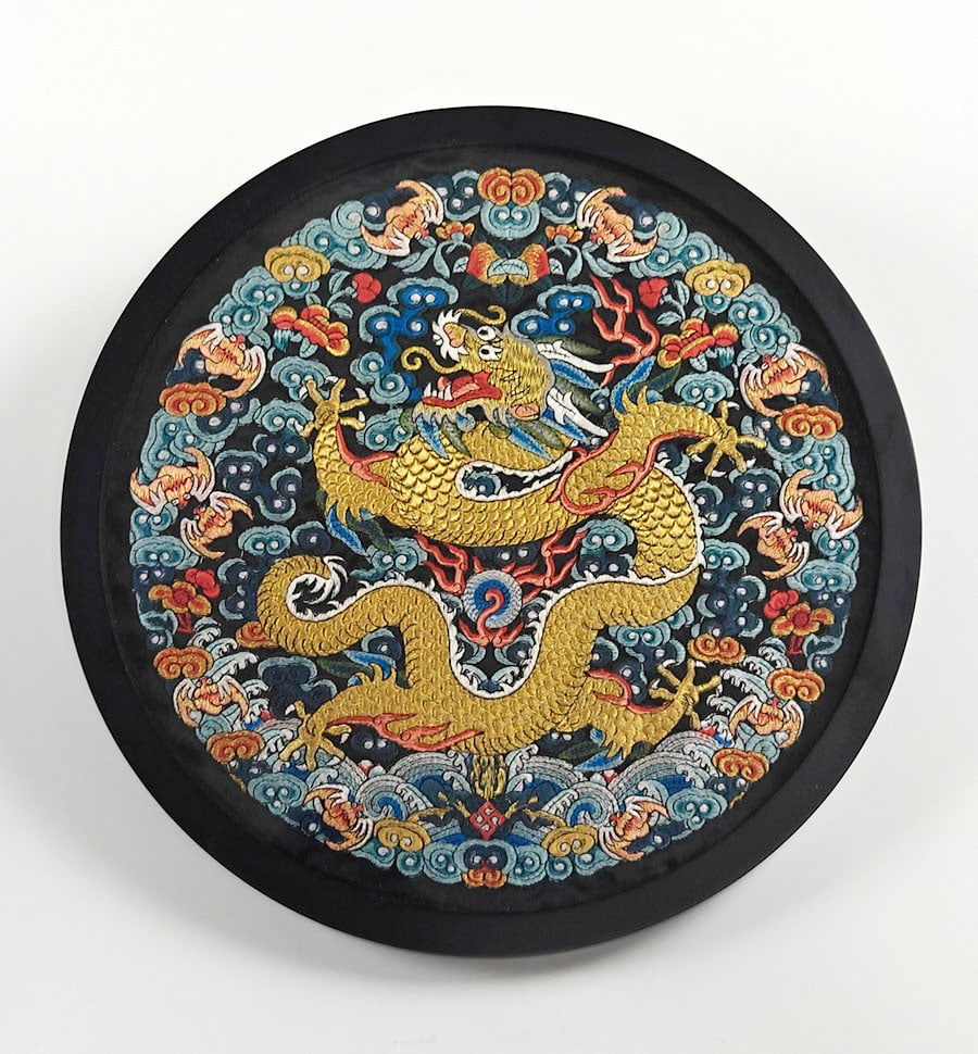Chinese Embroidered Dragon Roundel: A circular embroidered textile panel worked with a sinuous five-clawed gilt dragon amid scrolling clouds, bats, waves and auspicious emblems. The design is rendered in shades of gold, turquoise,