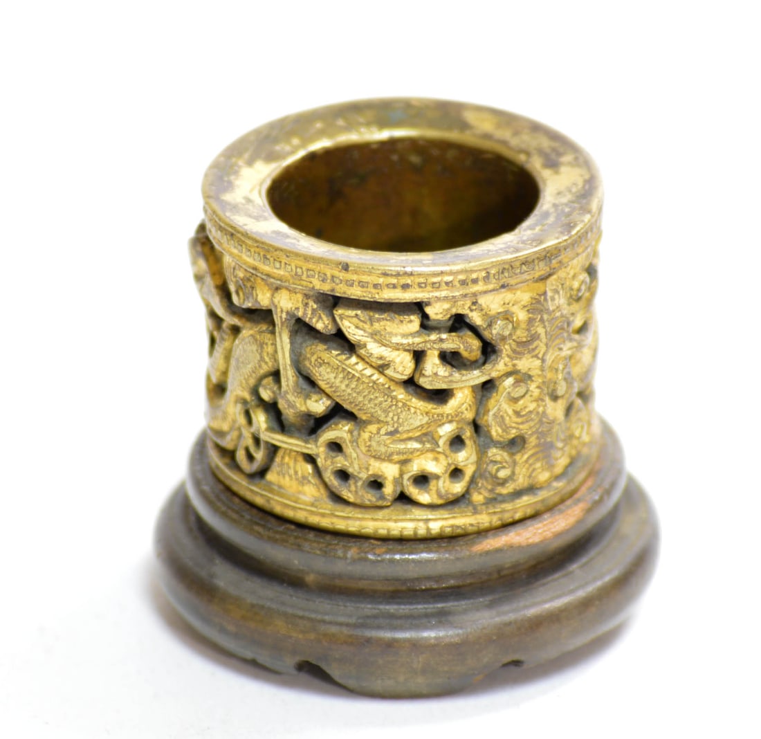 Chinese Gilt-Metal Dragon Arther's Ring: The cylindrical gilt-metal ring is cast and pierced with a continuous procession of writhing dragons and other mythical beasts amid cloud scrolls. It is finished with narrow geometric borders at the